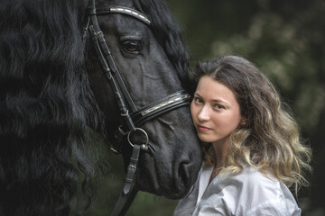 Beautiful young lady posing with a purebred friasian horse in the forest. - 459062564