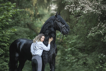 Beautiful young lady posing with a purebred friasian horse in the forest. - 459062565