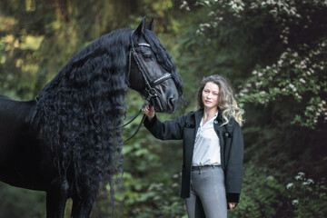 Beautiful young lady posing with a purebred friasian horse in the forest. - 459062594