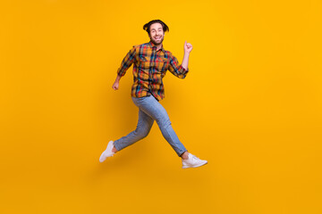 Fototapeta na wymiar Full body photo of crazy brunet young guy run wear shirt jeans sneakers isolated on yellow background