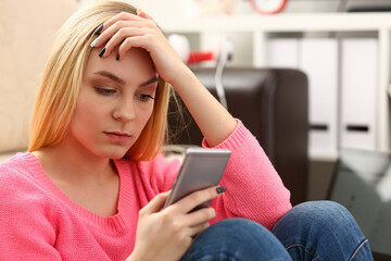 young pretty blond womansit on sofa hold smartphone in hands