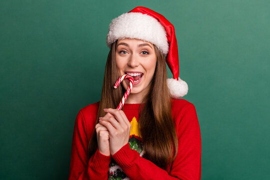 Photo of young woman happy positive smile eat candy yummy wear santa hat isolated over green color background