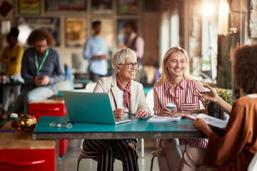Female colleagues are having a good time while sitting at desk in the office and chatting