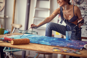 A young sexy and attractive female artist is enjoying the music while painting in her studio. Art, painting, studio