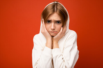 Young doubtful beautiful dark blonde woman with sincere emotions isolated on background wall with copy space wearing casual white hoodie looking at camera