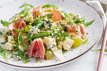 Salad of pear, blue cheese, grape, prosciutto, arugula and nuts with spicy dressing on a light background. Healthy eating.