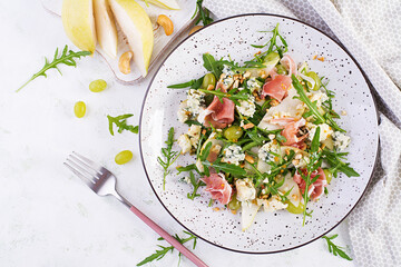 Salad of pear, blue cheese, grape, prosciutto, arugula and nuts with spicy dressing on a light...