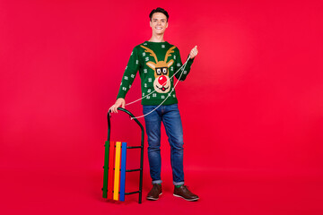 Full length body size photo happy guy in ugly sweater smiling with sledges isolated bright red color background