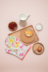 wooden set of potholder butter, 
red currant, jug of milk, flour, broken raw egg, on the light red background 
