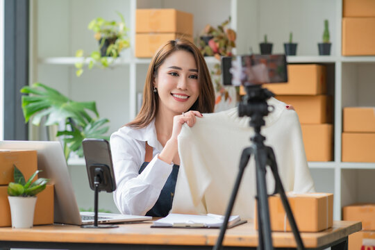 Young Asian woman entrepreneur talking camera live recording video on the social network at home. Online selling, work from home, business, and technology concept