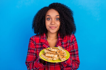 Photo of cute young brunette lady hold sweets wear red checkered pajama isolated on blue color...