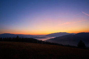 Nice autumn sunrise in the mountains. The sun hid behind the mountain. The fog lies in the low