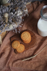 Composition with cookies on a wooden board, milk in a glass bottle and a basket with lavender and spikelets