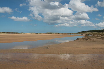 Landscape of beautiful sandy beach with no people and sands stretched to horizon with white puffy clouds reflected in the water pools in Holkham north Norfolk East Anglia uk
