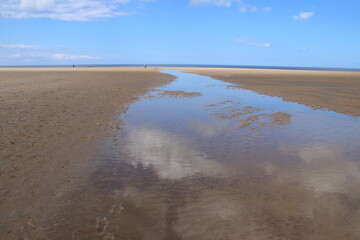 Obraz premium Landscape of beautiful sandy beach with no people and sands stretched to horizon with white puffy clouds reflected in the water pools in Holkham north Norfolk East Anglia uk