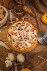 Pizza with ham and mushrooms on a board surrounded by fresh ingredients top view