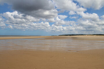 Landscape of beautiful sandy beach with no people and sands stretched to horizon with white puffy clouds reflected in the water pools in Holkham north Norfolk East Anglia uk