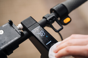 A woman's hand with a manicure wipes the display of an electric scooter with a wet wipes, the display shows the battery charge.