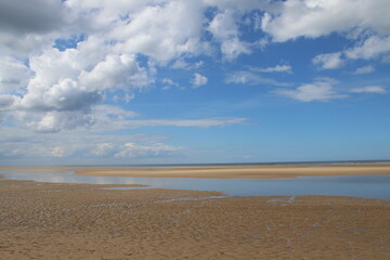 Landscape of beautiful sandy beach with no people and sands stretched to horizon with white puffy clouds reflected in the water pools in Holkham north Norfolk East Anglia uk