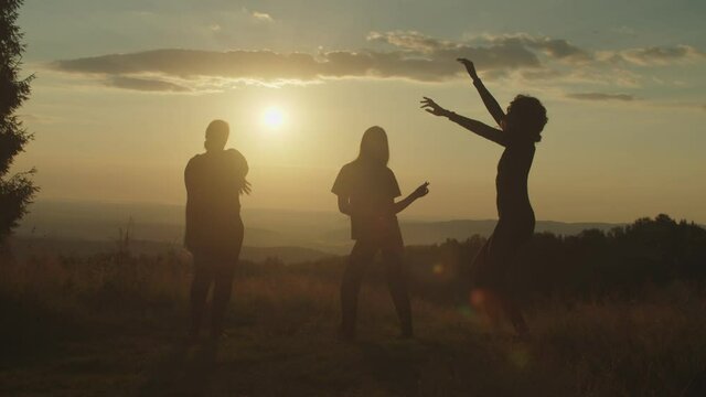 Silhouette of elegant attractive multiracial women having fun , dancing gracefully, enjoying recreation and freedom, expressing carefree mood, positivity and happiness on mountain top at sunset.