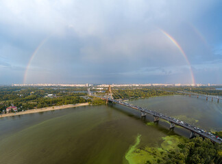 Fototapeta na wymiar Rainbow over the North Bridge in Kiev. Green algae bloom in the water of the Dnieper River. Aerial drone view.