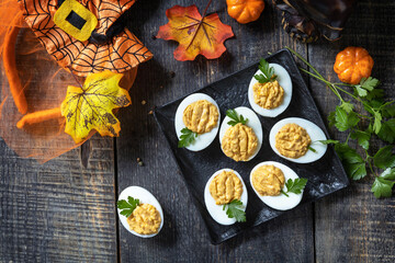 Halloween funny idea for party food. Halloween creative set stuffed eggs pumpkin on a wooden table. Top view flat lay background.