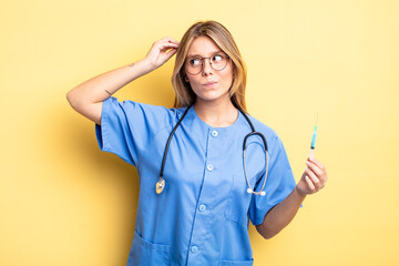 pretty blonde girl feeling puzzled and confused, scratching head. nurse an vaccine concept
