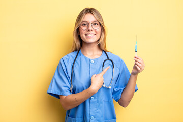 pretty blonde girl smiling cheerfully, feeling happy and pointing to the side. nurse an vaccine concept - obrazy, fototapety, plakaty