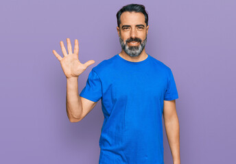 Middle aged man with beard wearing casual blue t shirt showing and pointing up with fingers number five while smiling confident and happy.