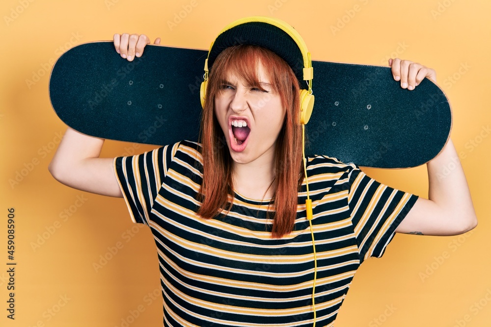 Canvas Prints redhead young woman holding skate wearing headphones angry and mad screaming frustrated and furious,