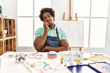 Young african american man sitting on the table at art studio thinking looking tired and bored with depression problems with crossed arms.