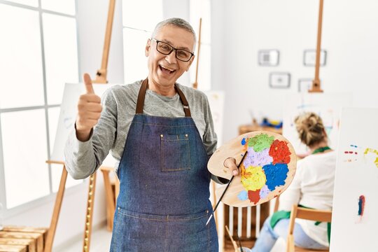 Middle age caucasian man drawing canvas at art studio smiling happy and positive, thumb up doing excellent and approval sign