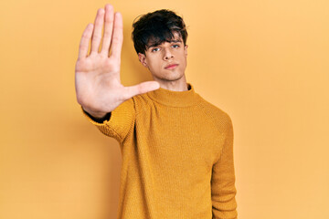 Handsome hipster young man wearing casual yellow sweater doing stop sing with palm of the hand. warning expression with negative and serious gesture on the face.