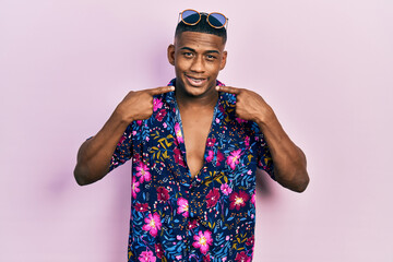 Young black man wearing hawaiian shirt and sunglasses smiling cheerful showing and pointing with fingers teeth and mouth. dental health concept.