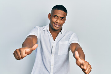 Young black man wearing casual white shirt approving doing positive gesture with hand, thumbs up smiling and happy for success. winner gesture.