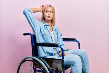 Beautiful blonde woman sitting on wheelchair confuse and wondering about question. uncertain with...