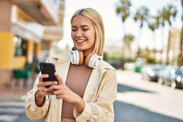 Young blonde girl smiling happy using smartphone and headphones at the city.