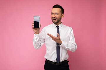 Photo of handsome smiling adult male person good looking wearing casual outfit standing isolated on background with copy space holding smartphone showing phone in hand with empty screen display for