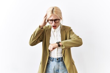 Beautiful caucasian business woman standing over isolated background looking at the watch time...