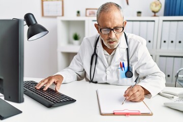 Senior grey-haired man wearing doctor uniform working at clinic