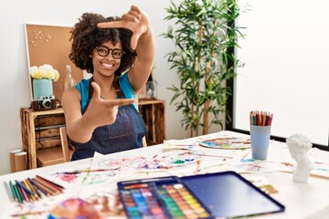 Beautiful african american woman with afro hair painting at art studio smiling making frame with hands and fingers with happy face. creativity and photography concept.
