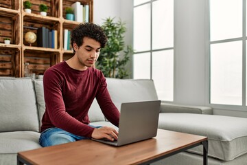 Young hispanic man using laptop sitting on the sofa at home.