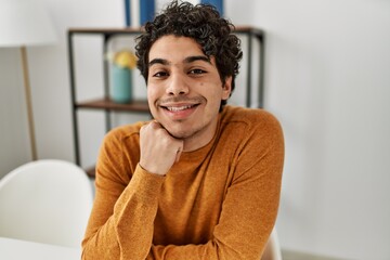 Young hispanic man smiling happy sitting on the table at home.