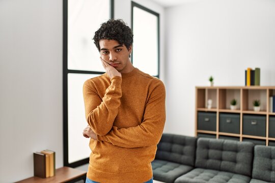 Young hispanic man wearing casual clothes standing at home thinking looking tired and bored with depression problems with crossed arms.