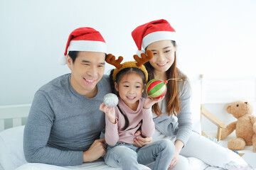 Asian family celebrating Christmas wearing red Santa Claus hat with decorative gifts and gift boxes or present in bedroom, holiday in festive Merry Christmas or X'mas and happy new year concept