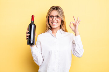 pretty blonde girl feeling happy, showing approval with okay gesture. wine bottle concept