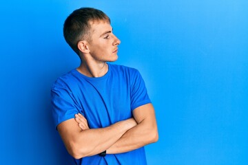 Young caucasian man wearing casual blue t shirt looking to the side with arms crossed convinced and confident