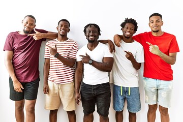 Young african group of friends standing together over isolated background cheerful with a smile on face pointing with hand and finger up to the side with happy and natural expression