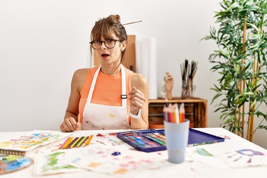 Hispanic woman at art studio scared and amazed with open mouth for surprise, disbelief face