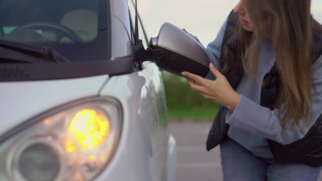 Broken off side rearview mirror on car. Woman is checking for damage on her auto